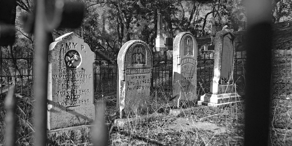 4 tombstones are viewed through a cemetery gate