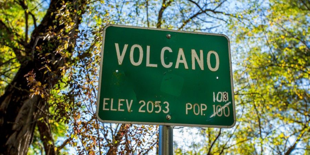 City sign for Volcano CA. Population of 100 is crossed out with white ink and replaced with 103.