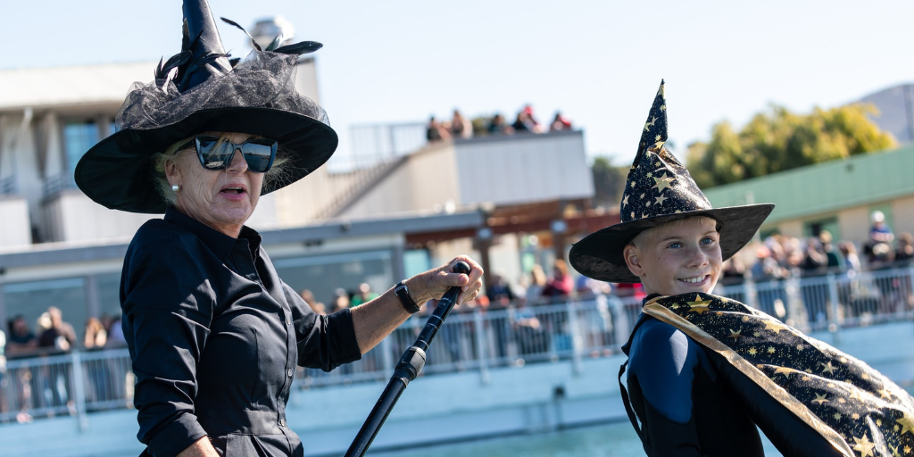 Fashionable grandmother in sunglasses and witches hat paddles with grandson in wizard costume. Grandson