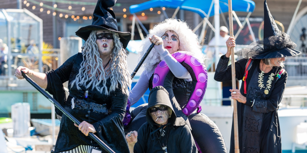 Four witches in full costume float together the water, paddles in hand.