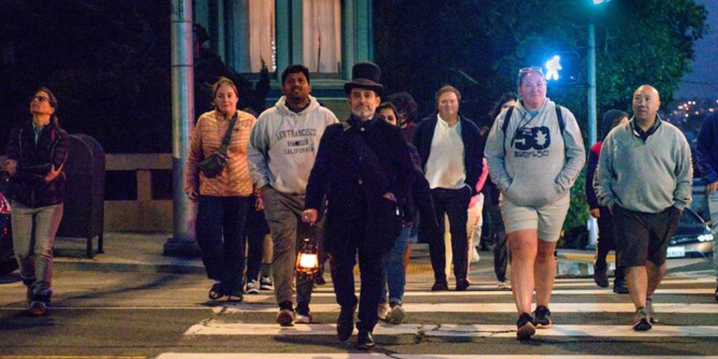 Group of men cross the street at night while following behind a man wearing a top hat